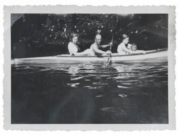 Three adults and one child are sitting in a canoe and paddling on the water