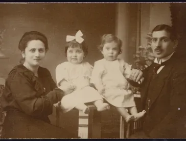 An old black-and-white family photo. On the left is a woman (the mother). In the middle are two small children. On the right is a man (the father).