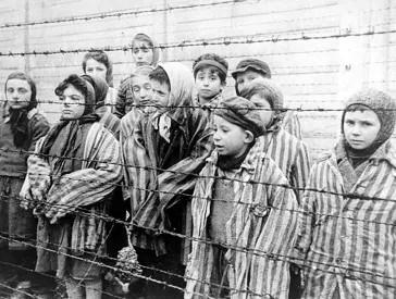 Black and white photograph with children in concentration camp clothes in Auschwitz standing behind barbed wire fence