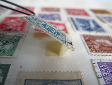 Tweezers lift stamp in an album.