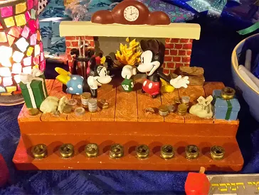 Der im Text beschriebene Chanukka-Leuchter auf einem Tisch mit Geschenken, Lampe und Dreidel.