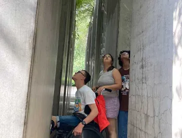 The picture shows three teenagers, one of them using a wheel chair. They are squeezed in between blocks of concrete and looking upwards.