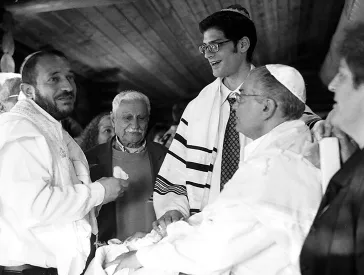 Black and white photo: four men with kippas standing around a baby.