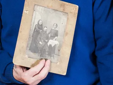 An elderly couple holding an old black and white photograph in their hands.