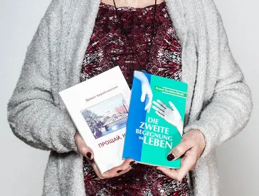 Two hands with dark red nail polish holding two books.