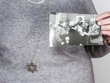 A woman leans on a walking stick and holds two photos in her hand.