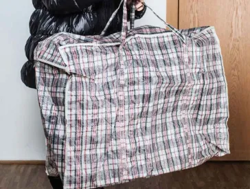 A woman in a thick winter jacket carries a huge plaid plaid bag.