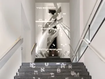 Stairway to the permanent exhibition.Hebrew and Latin letters are projected onto the steps, which combine to form town names at the top of the stairs