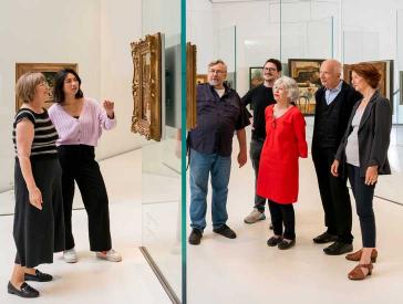 Visitors in an exhibition room with paintings on glass walls.