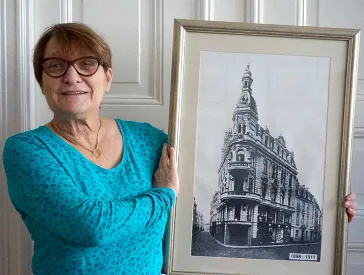 A woman holds a picture with a building view into the camera.