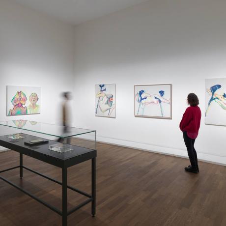 Person with a red sweater looks at paintings on the walls of an exhibition room.