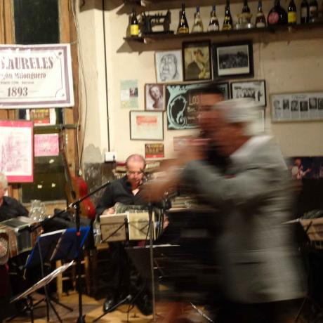 View into a dance hall. A couple dancing in the foreground out of focus, musicians sitting behind microphones and music stands in the background.