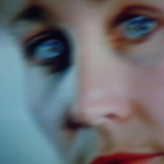 Blurred close-up of a face with very blue eyes and a red mouth.