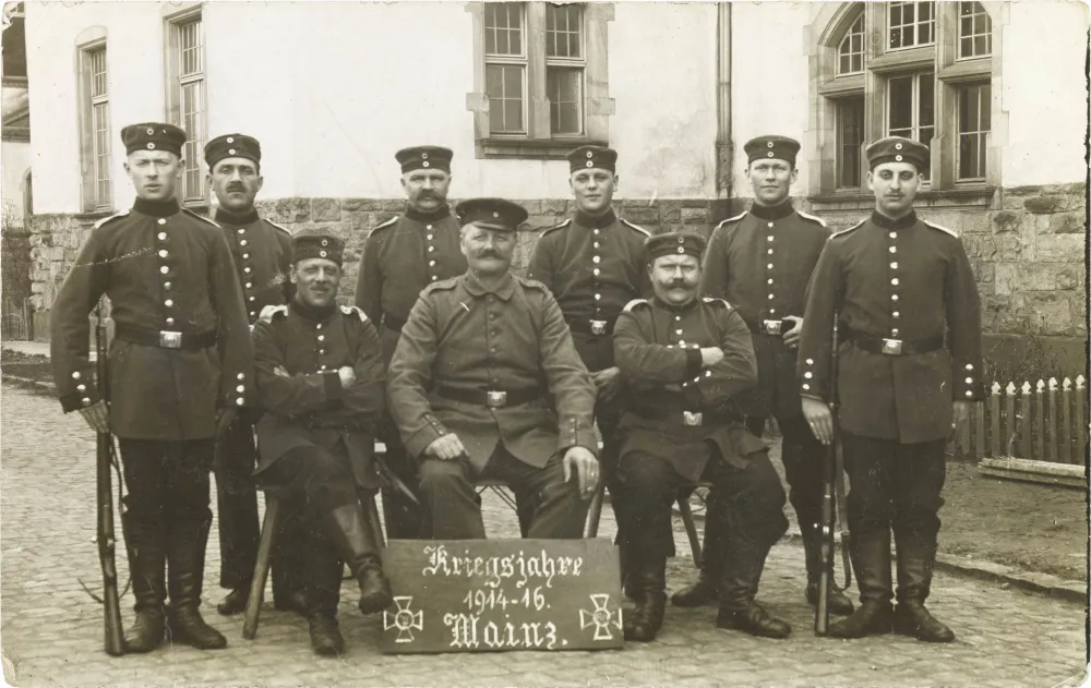 Black and white photo: Nine uniformed soldiers in front of barracks