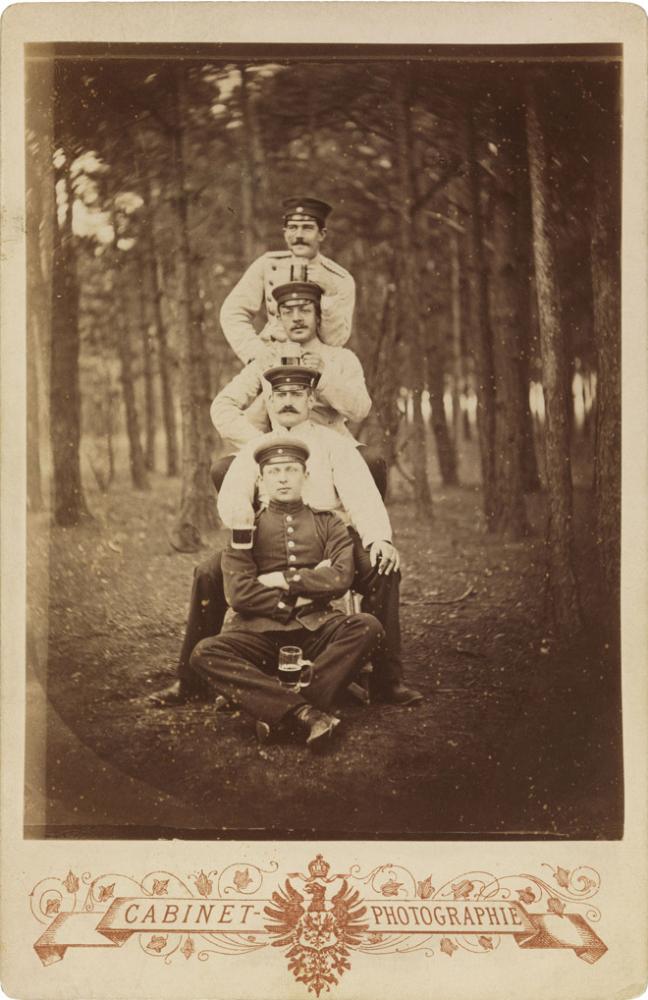 Black-and-white photograph: Four uniformed soldiers with beer mugs in a wooded area