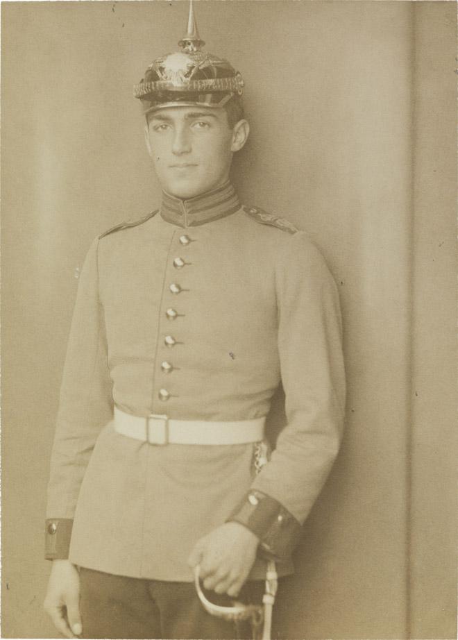 Schwarz-weiß-Foto: Junger Mann in Soldatenuniform mit weißem Gürtel, Pickelhaube und Degen, Atelieraufnahme