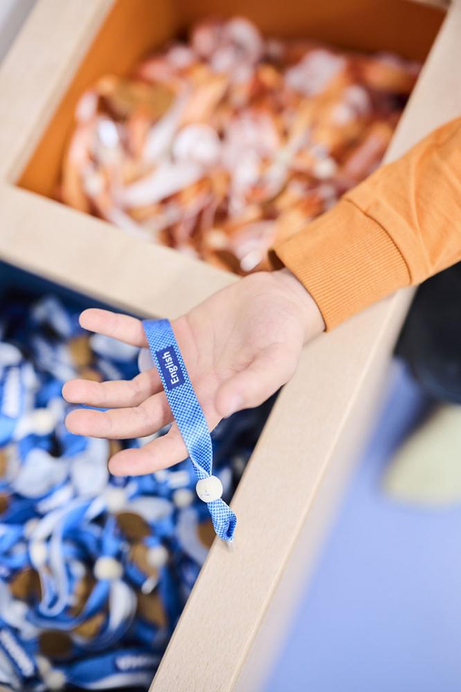 Die Kinderhand ergreift ein blaues Band mit der Aufschrift "English".