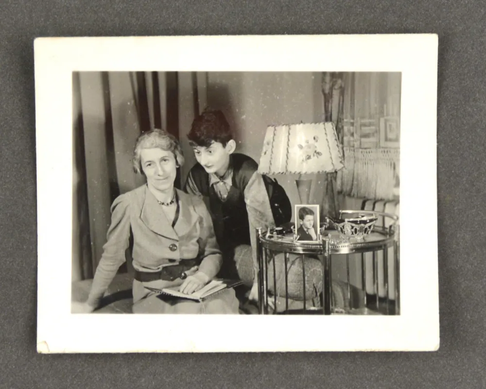 A woman and a child next to a small table with a floor lamp, on the table is a photo portrait of a boy.