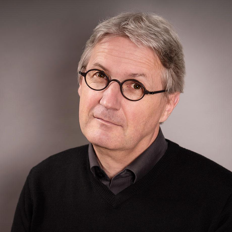 A man with small black glasses and short gray hair looks friendly into the camera.