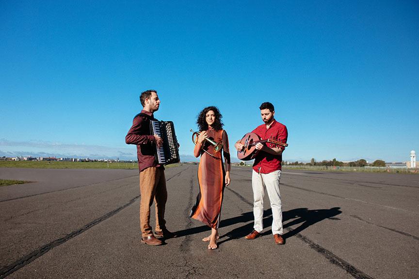 A man with an accordion, a woman with a trumpet and a man with a guitar are standing on Tempelhof Field. 