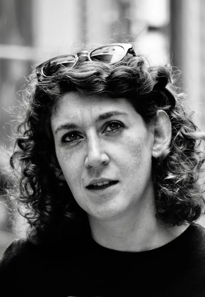 Black and white portrait of a woman with half-length curls and glasses in her hair, looking diagonally upwards.