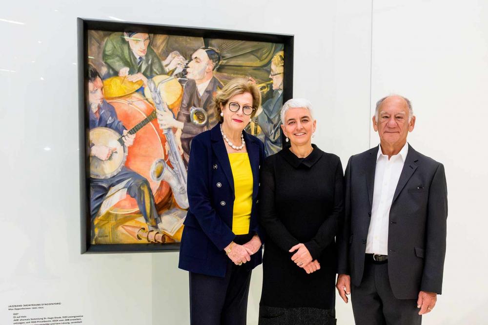 Three people are standing in front of a painting of a jazz band.