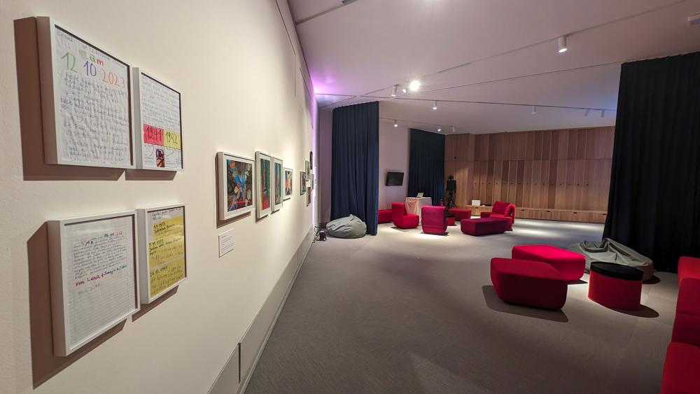 View into a windowless room with red upholstered furniture, gray beanbags, black curtains as room dividers and picture frames on a white wall.