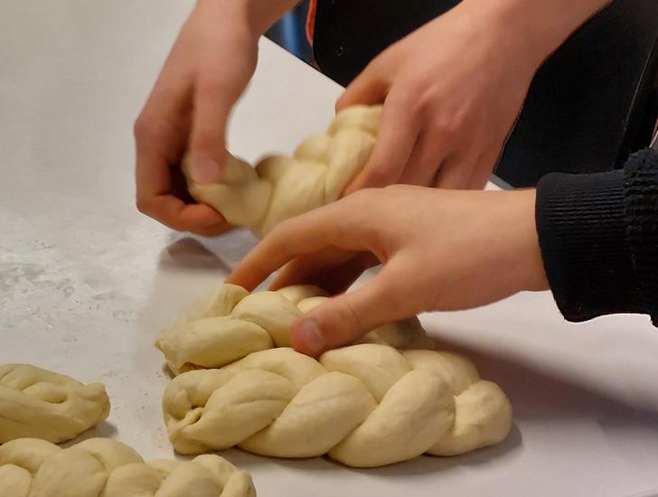 Hands make plaits of dough on a table.