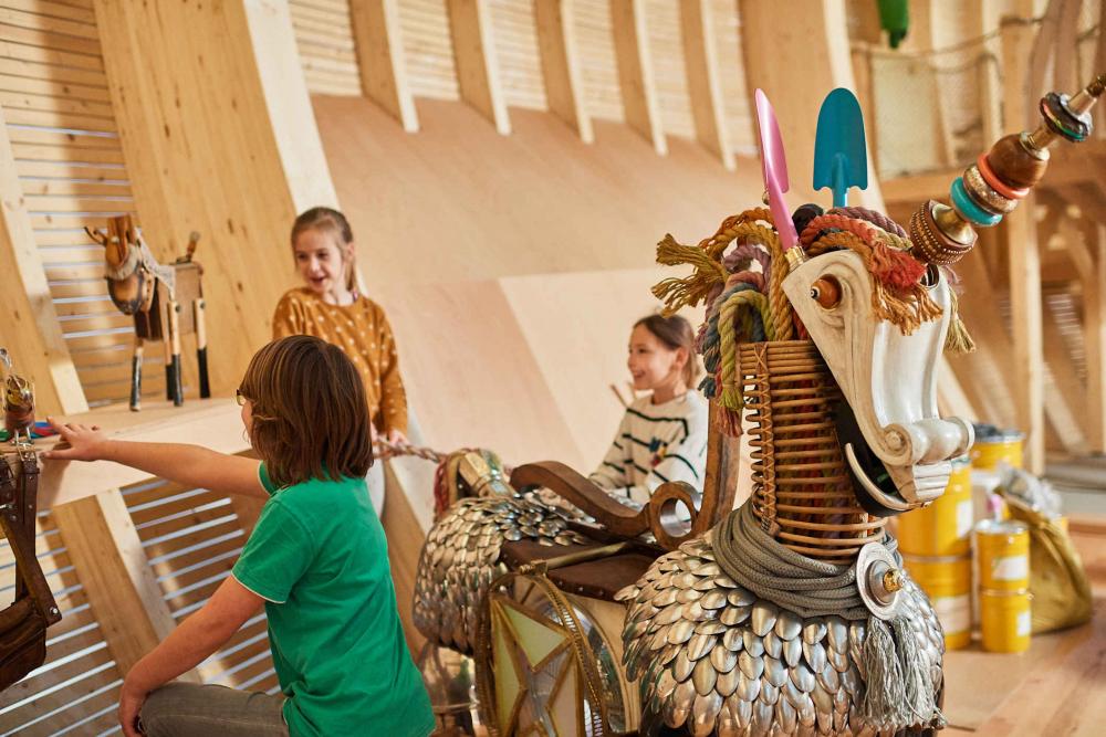 Ein aus Löffeln, Schaufeln und anderen Elementen gebautes Einhorn hinter dem Kinder stehen und spielen