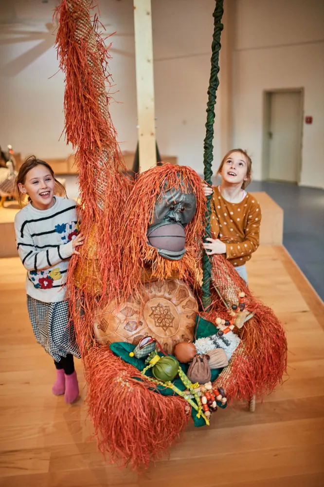 Two children stand next to an orangutan made of everyday objects