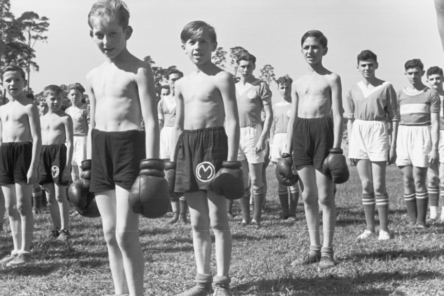 Kinder die aufgereiht auf einer Wiese stehen. Sie tragen Sportkleidung und Boxhandschuhe