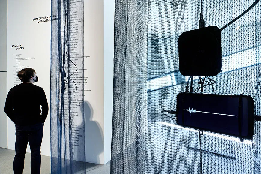 Room view of the exhibition with visitor, in the foreground a screen with a voice wave