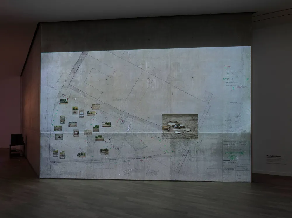 View of an exhibition wall with a large section of a city map and photos glued to it.
