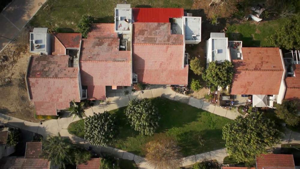 Bird’s eye view of several row houses with red roofs. They are surrounded by trees, front gardens and driveways.