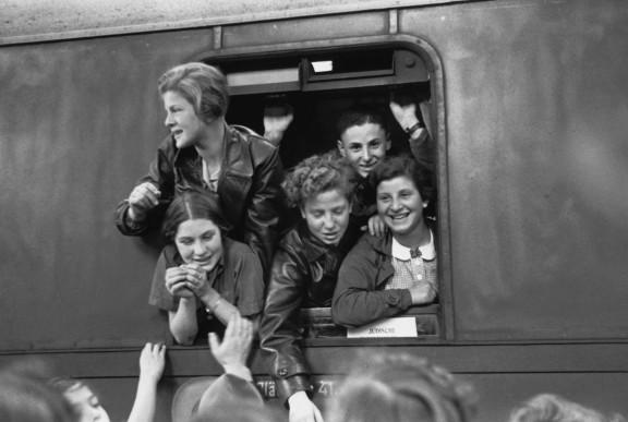 Schwarz-Weiß-Fotografie jugendlicher Jungen und Mädchen, die sich lachend aus einem Zugfenster lehnen