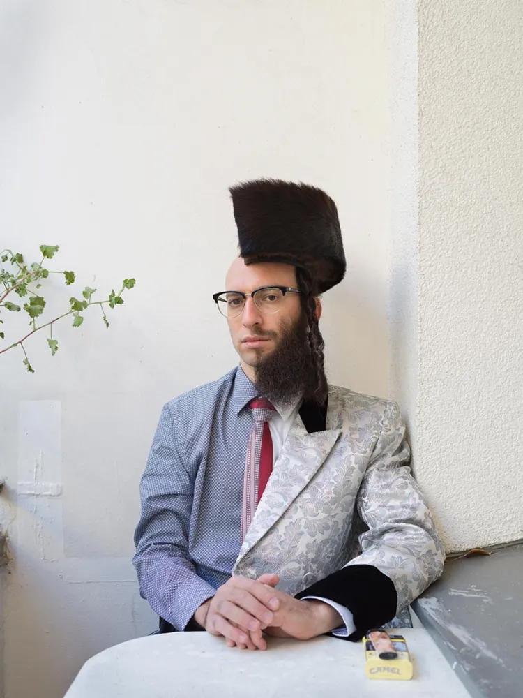 Photograph of a man divided along the longitudinal axis, as it were, into two halves: on the left side he wears a shirt and bald head, on the right a full beard and a (halved) shtreimel on his head