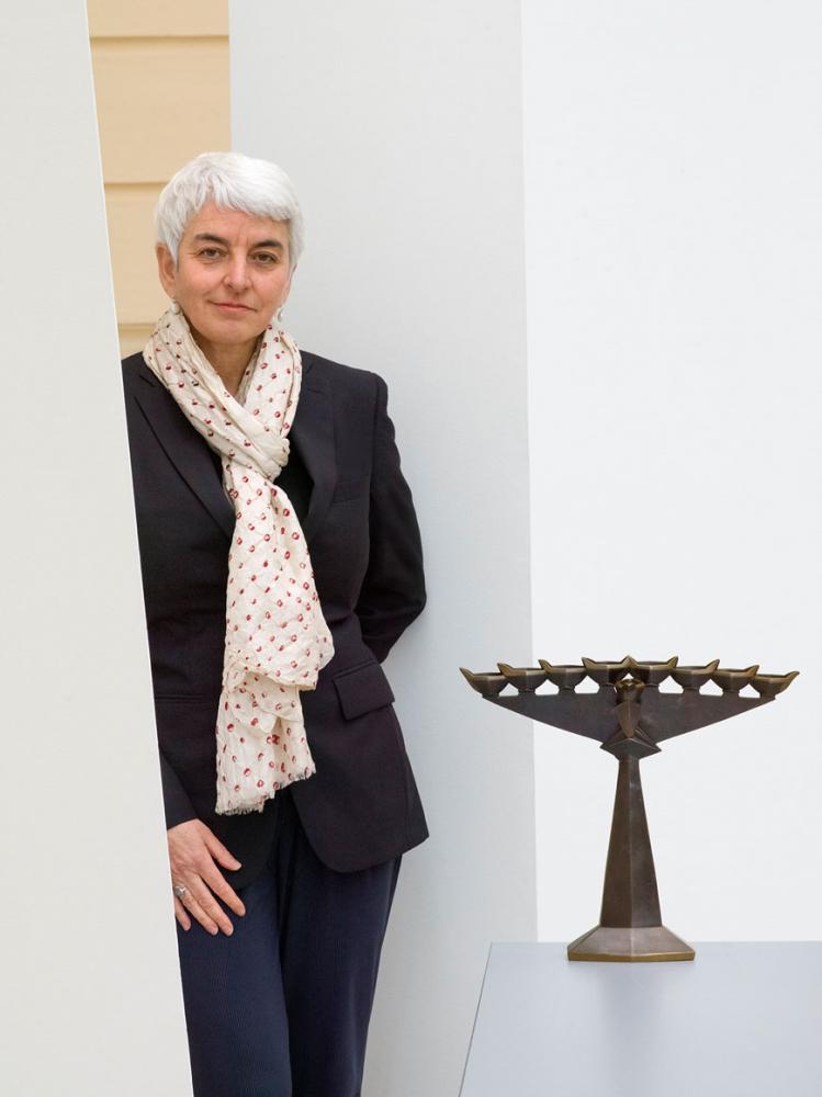 Hetty Berg stands in front of white background next to the candlestick