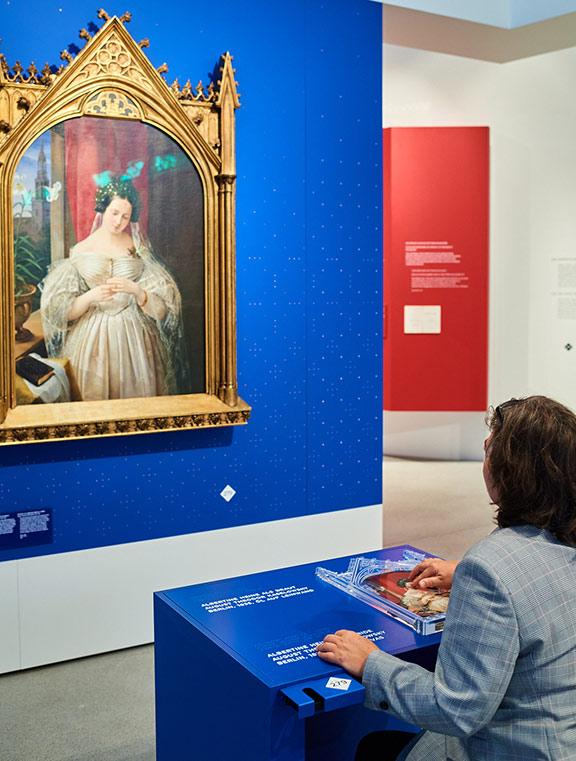 Eine Person fährt mit den Fingern über einen Tastplan, an der Wand vor ihr das Ölgemälde einer Braut