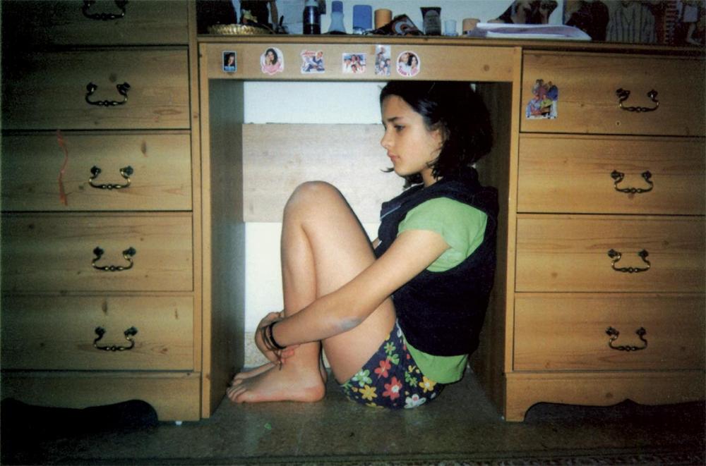 Girl in shorts crouches under a desk