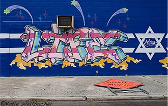 Graffiti written with spray paint on a blue wall, the Star of David is drawn next to the graffiti words