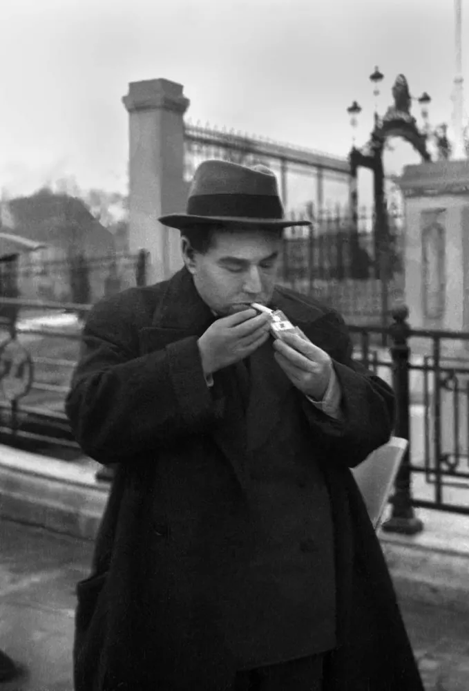 Black-and-white portrait of Egon Erwin Kisch, who is lighting a cigarette on the street