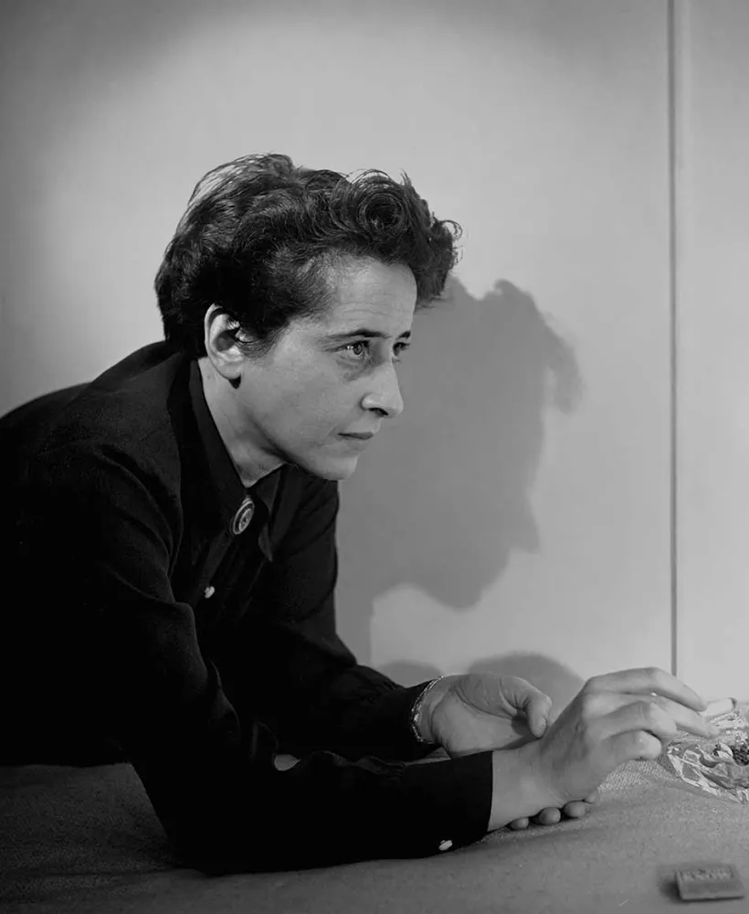 Black and white portrait of Hannah Arendt wearing a dark collar shirt leaning over an ashtray