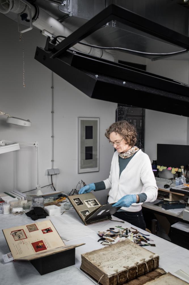 A woman with blue rubber gloves standing at a desk, looking through old pictures.