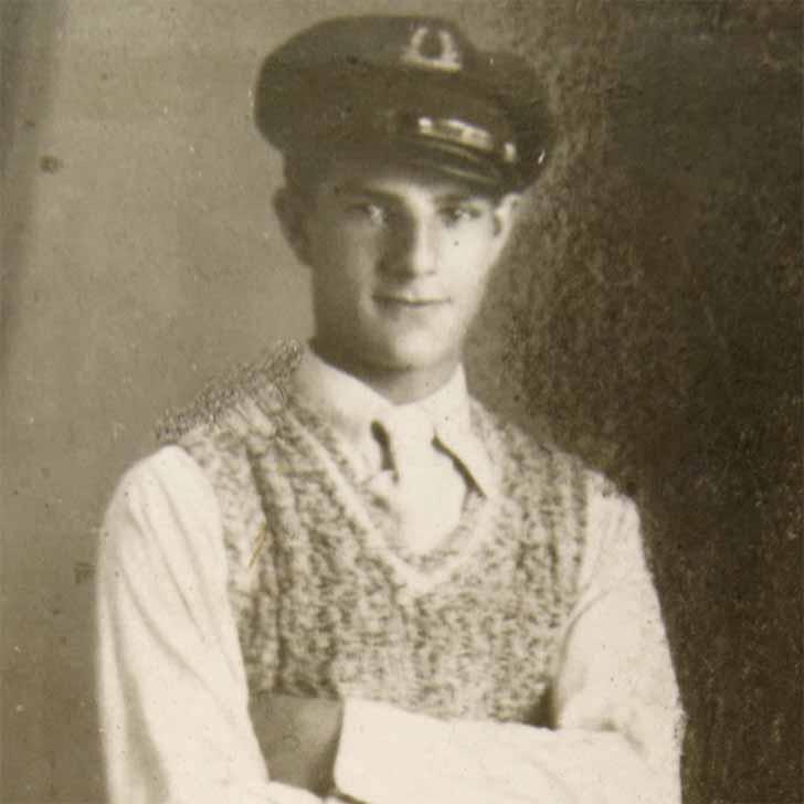 Portrait of a standing young man in a sailor's cap and a hand-knit sweater. He has a friendly look on his face and a delicate build.