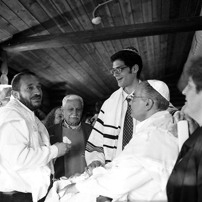 Black and white photography: Grandfather and father look at the mohel, the great-granduncle at the baby