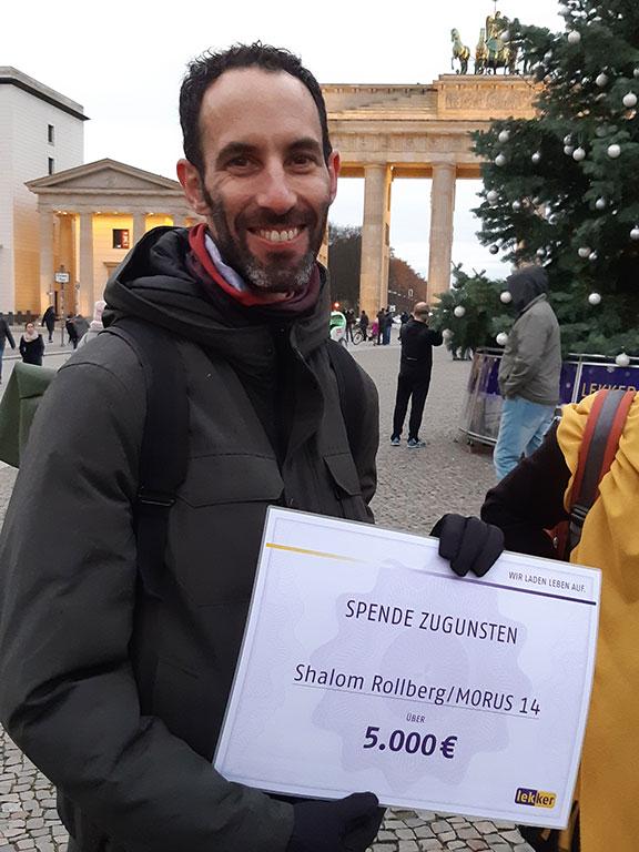 Man smiling at the camera, holding a check for 5,000 euros