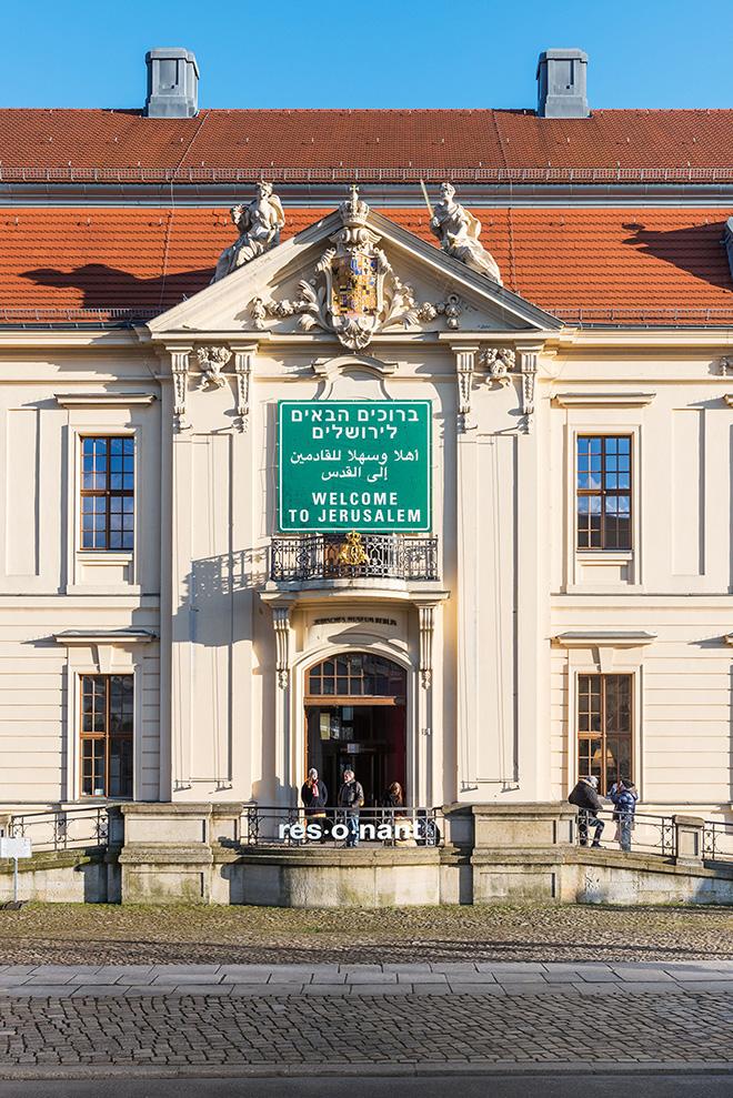 Auf dem Farbfoto ist die Fassade des Jüdischen Musuems Berlin mit dem einem Verkehrsschild nachempfundenen Schild mit der Aufschrift Welcome to Jerusalem in den Spachen Englisch, Arabisch und Hebräisch zu sehen.