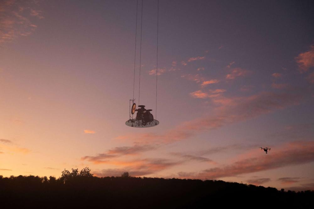 Sonnenuntergang, Trommeln mit Schlagzeugern auf einer runden Platte, die an Fäden durch den Himmel schwebt.