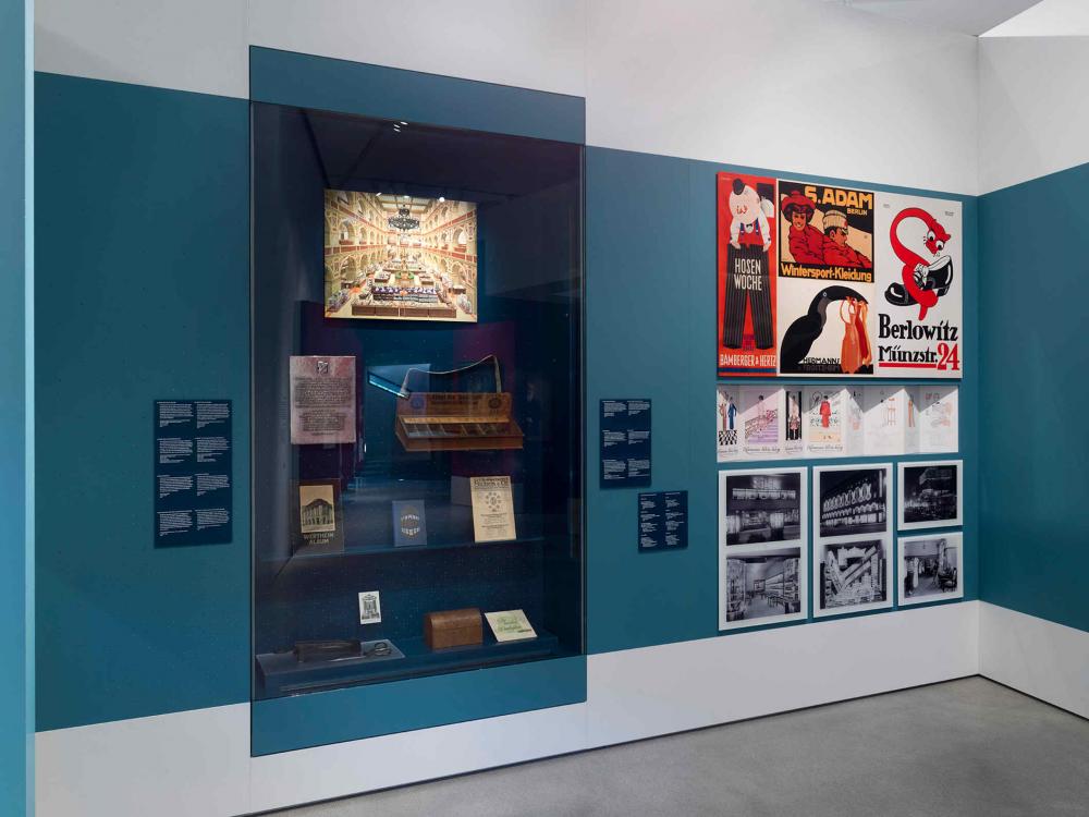 Vitrine mit Ausstellungsobjekten und Plakate an einer blauen Wand