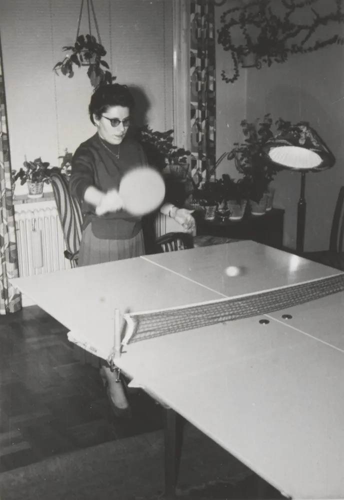 Eine Frau spielt Pingpong, im Hintergrund eine Stehlampe.